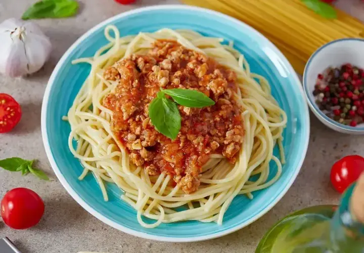 Spaghetti bolognese na talerzu, ozdobione bazylią. Idealne na prosty przepis obiadowy.