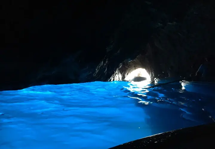 Acqua azzurra e luminosa in una grotta buia, con un'uscita illuminata dove si intravede una barca.