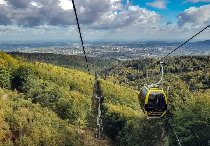 Żółta kolejka linowa z Szyndzielni na Klimczok mija jesienne lasy, a w oddali widać panoramę miasta.