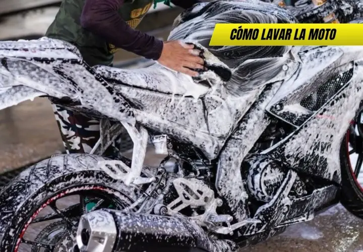 Persona lavando una moto deportiva con espuma. Se ve el motor, la rueda trasera y el tubo de escape. ¡Así se limpia la moto!