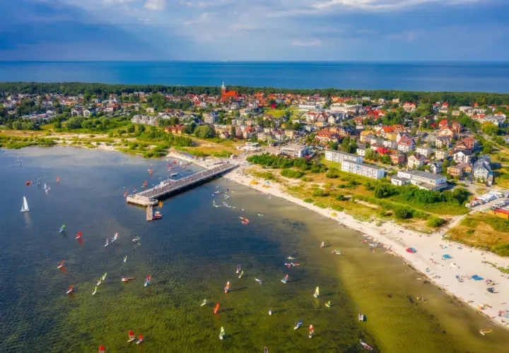 Jastarnia atrakcje dla dzieci: widok na molo, plażę i zatokę pełną żaglowców i desek windsurfingowych.