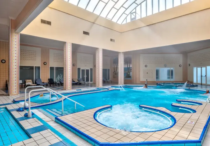Wnętrze basenu z hydromasażem w Mahdia Palace. Woda jest turkusowa, a wokół basenu znajdują się leżaki.