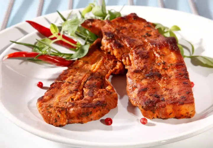 Dwa soczyste kawałki boczku z grilla, przyprawione i udekorowane papryczkami chili i zieleniną.