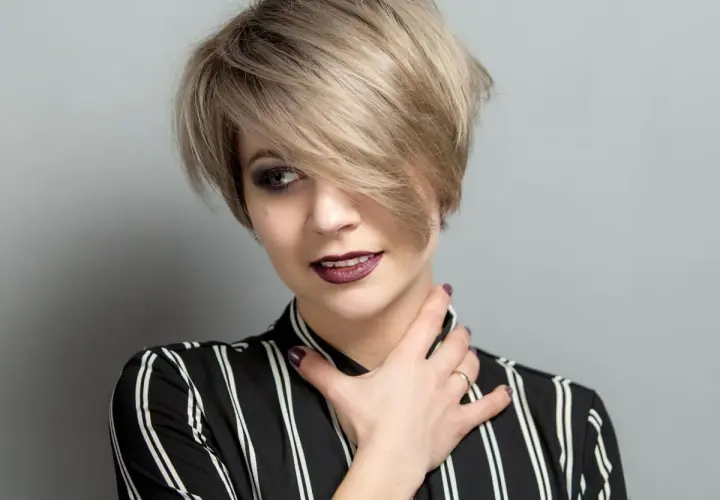 Kobieta z krótkimi blond włosami w stylu pixie, z grzywką na bok, w bluzce w paski.