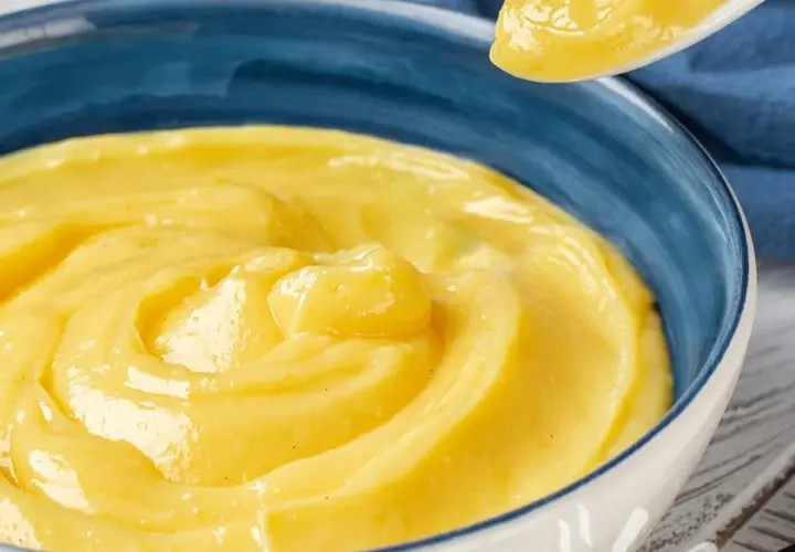 Una ciotola blu piena di deliziosa crema pasticcera vegana, con un cucchiaio che ne preleva una porzione.