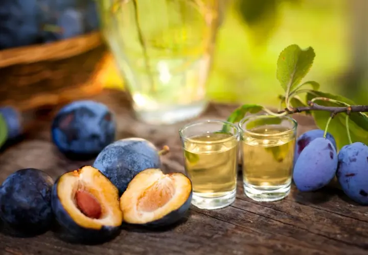 Jak przygotować domową nalewkę na whisky z suszonymi śliwkami? Dojrzałe śliwki i dwa kieliszki złocistego trunku na drewnianym stole.