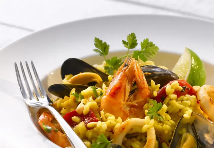 Pyszne risotto z owocami morza: krewetki, małże, kalmary i ryż, udekorowane natką pietruszki i ćwiartką limonki.