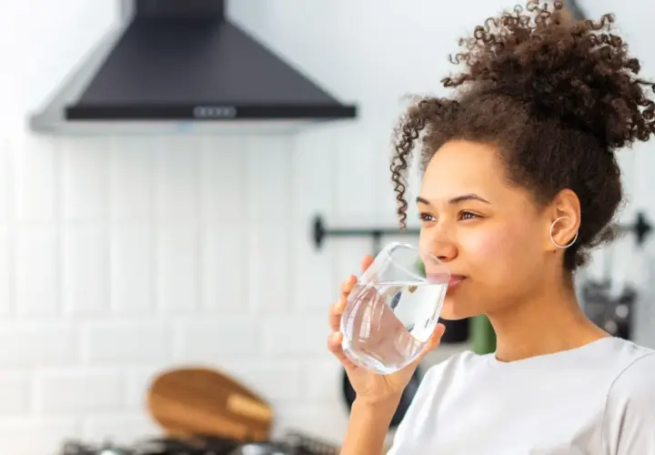 Donna sorseggia un bicchiere d'acqua, un rimedio naturale per la stitichezza.
