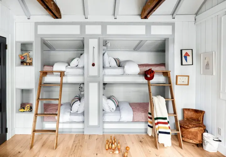 A cozy built in bunk room with four beds, wooden ladders, and playful decor like toy excavators and bowling pins.