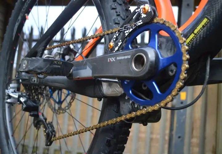 Close-up of a mountain bike's drivetrain, featuring a SRAM XX1 chain, blue chainring, and black crank arm.