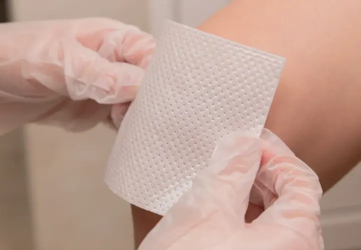 Ręce w rękawiczkach przygotowują plastry z opatrunkiem na rany pooperacyjne do aplikacji.