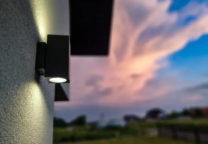 Nowoczesny kinkiet oświetla ścianę domu. To dobry przykład, jak załatwić oświetlenie ulicy, tworząc przytulną atmosferę.