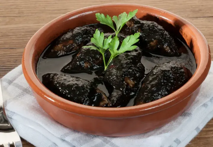 Chipirones en salsa negra, un plato tradicional servido en cazuela de barro, con perejil fresco y un tenedor al lado.