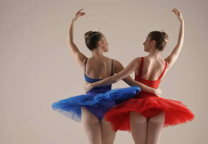 Due ballerine, una in blu e una in rosso, con tutù e diademi, si abbracciano durante un corso di danza per bambini.