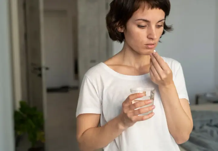 Mujer toma pastilla con agua, pensando en cuando tomar probióticos con antibióticos para cuidar su salud intestinal.