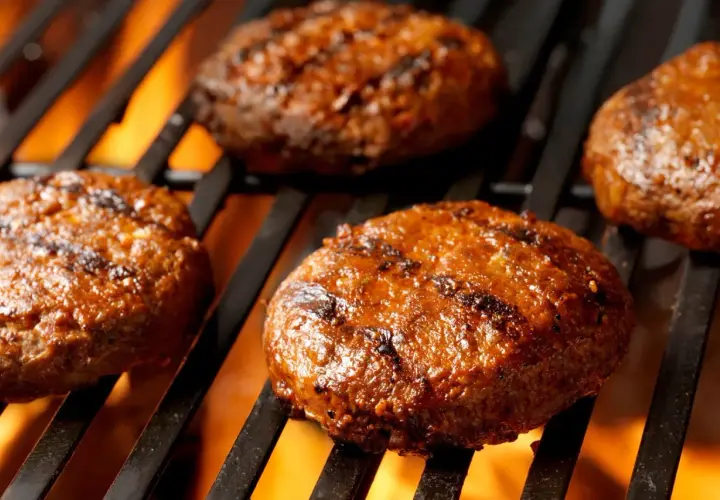Soczyste burgery z grilla pieką się na rozżarzonych węglach, tworząc apetyczne paski.