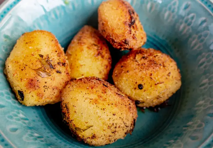 Fem gyllene, rostad potatis i ugn, kryddade med örter och peppar, serveras i en vacker turkos skål.