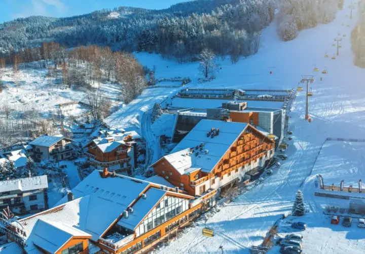 Idealne miejsce na ferie zimowe: ośnieżone góry, hotel z drewnianą elewacją i wyciąg krzesełkowy.