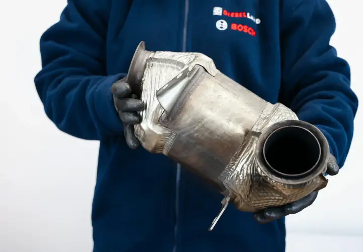 Mechanik w rękawiczkach trzyma filtr DPF. Czy DPF to katalizator? To pytanie często zadawane przez kierowców.