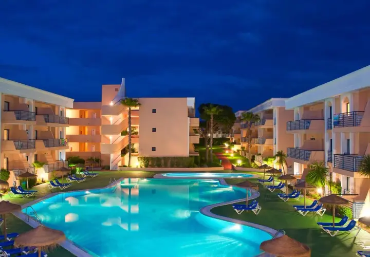 Resort con piscina iluminada y edificios de apartamentos bajo el cielo nocturno. Un lugar perfecto para disfrutar del sol Sancti Petri.