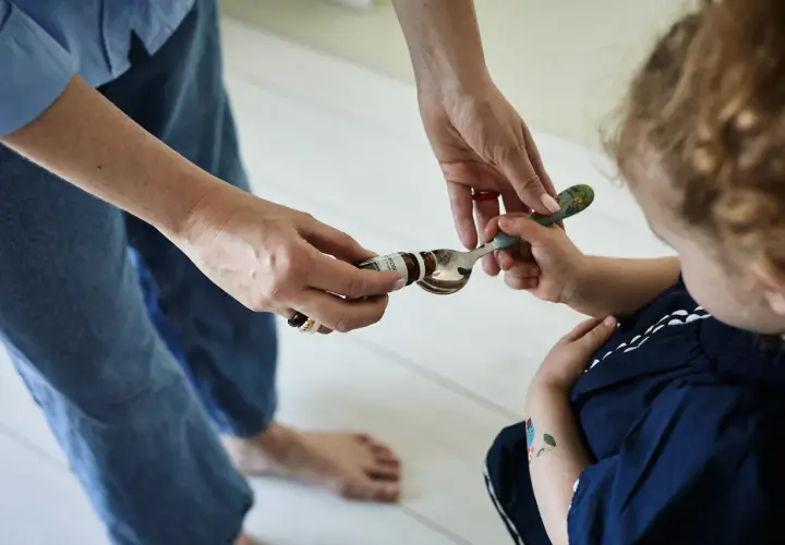 Mama podaje dziecku łyżeczkę z kroplami psychobiotyku. Dziecko z zaciekawieniem patrzy na podawany specyfik.
