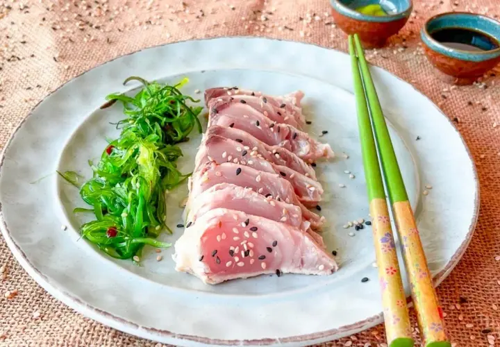Tataki de bonito, finas lonchas de pescado rosado con semillas de sésamo, acompañadas de ensalada de algas.