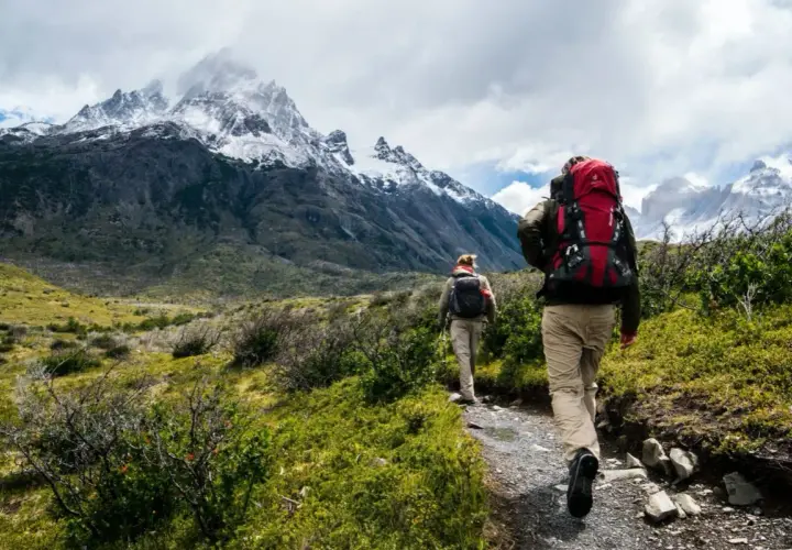 Dwie osoby z plecakami idą ścieżką w górach. To jest właśnie co to trekking – podróżowanie pieszo po trudnym terenie.