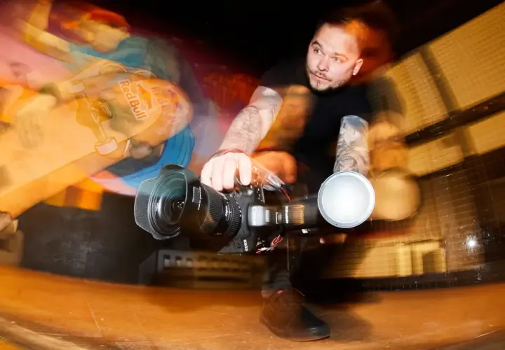 Zdjecie w ruchu: skater z deskorolką Red Bull i operator kamery z lampą błyskową.