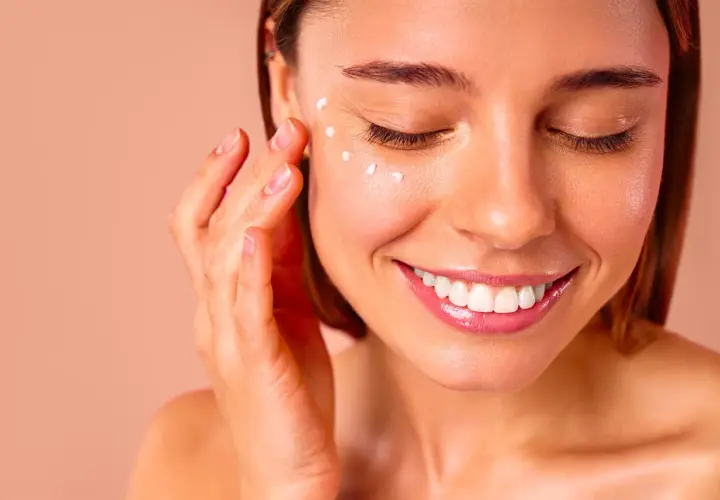 Une femme applique de la crème autour de ses yeux, un geste doux pour un massage des yeux relaxant.