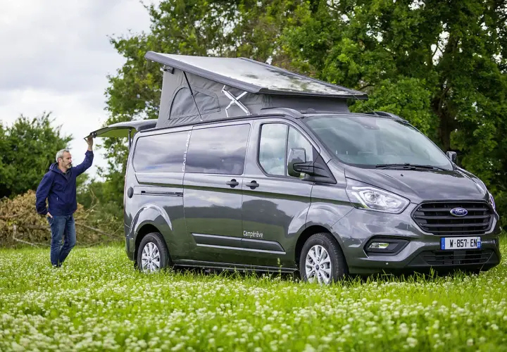 Un homme ouvre le hayon d'un van aménagé avec toilette, prêt pour l'aventure en pleine nature.