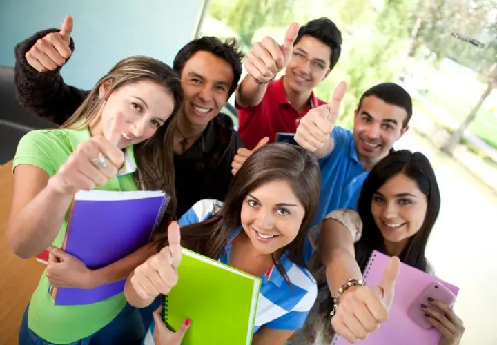 Uśmiechnięci studenci z notatnikami pokazują kciuki w górę, gotowi na studia stacjonarne.