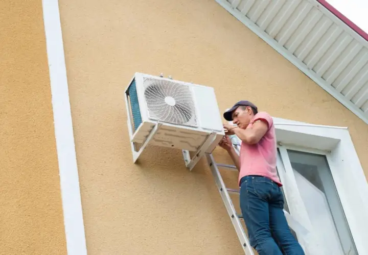 Técnico en escalera realizando la **instalación aire acondicionado exterior** en la pared de una casa.