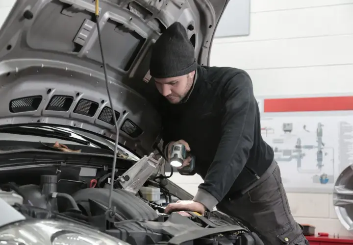 Mechanik z latarką bada silnik, szukając przyczyny, dla której samochód nie ma mocy.