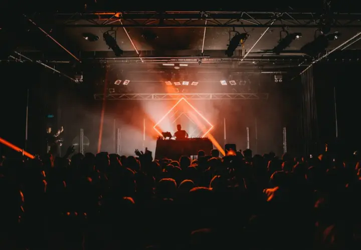 DJ set sous un éclairage orange vif, ambiance techno année 90. Foule en délire devant la scène.