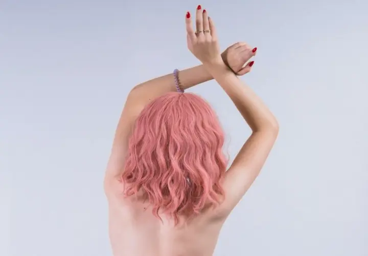 Kobieta z falowanymi włosami w odcieniu kolor magenta, z rękami skrzyżowanymi nad głową.