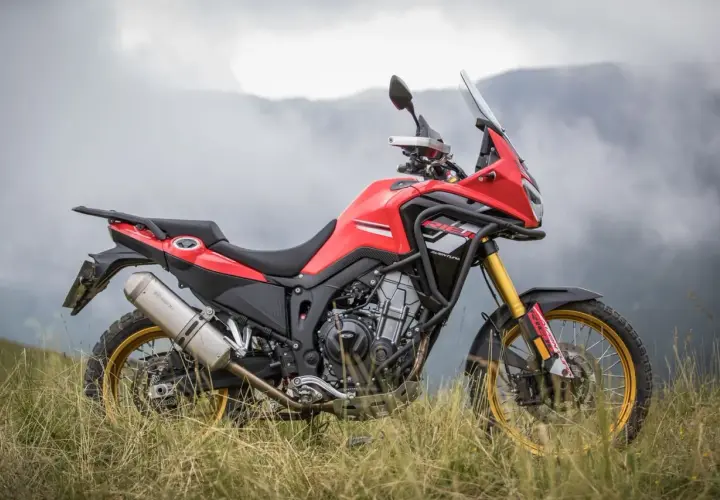 Rieju Aventura 500, lista para la aventura. Ficha técnica de esta moto trail roja y negra en un paisaje montañoso.