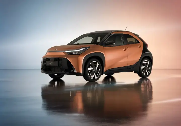 Pomarańczowy Toyota Aygo Cross z czarnymi akcentami i stylowymi felgami, odbijający się w lustrzanej podłodze.