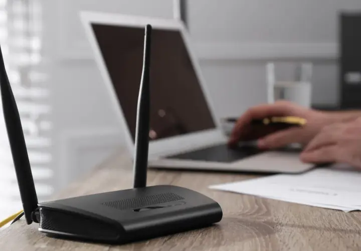 Router mit Antennen steht auf einem Holztisch. Ein Laptop hat kein WLAN mehr, der Nutzer versucht, das Problem zu lösen.