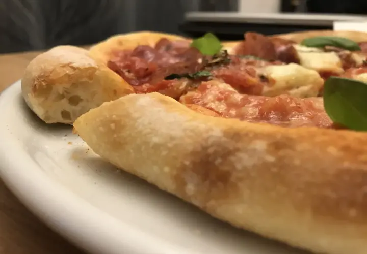 Nahaufnahme einer köstlichen Pizza mit dickem, luftigem Rand, belegt mit Tomaten, Käse und Salami. Ein echter Genuss, wie ein kleiner "pizza canotto".