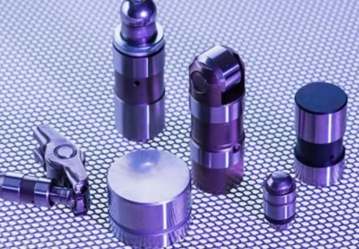 Varios taques hidráulicos de metal, algunos con forma cilíndrica y otros con un diseño más complejo, dispuestos sobre una superficie texturizada.