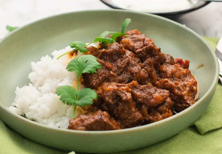 A bowl of lamb curry with rice and cilantro garnish.