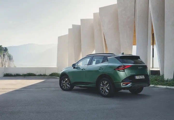 Zielony samochód Kia Sportage zaparkowany przed nowoczesnym budynkiem z elementami skalnymi w tle.