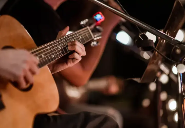 Ręce grające na gitarze akustycznej, w tle migoczą światła, tworząc atmosferę jak na stena line dyskotece.
