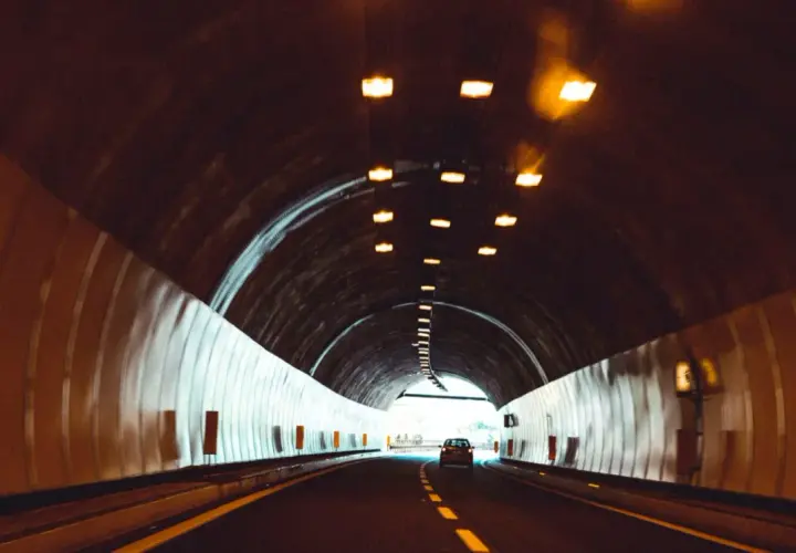 Samochód jedzie przez tunel, pokonując kolejne odległości w tunelu. Światła sufitowe oświetlają drogę.