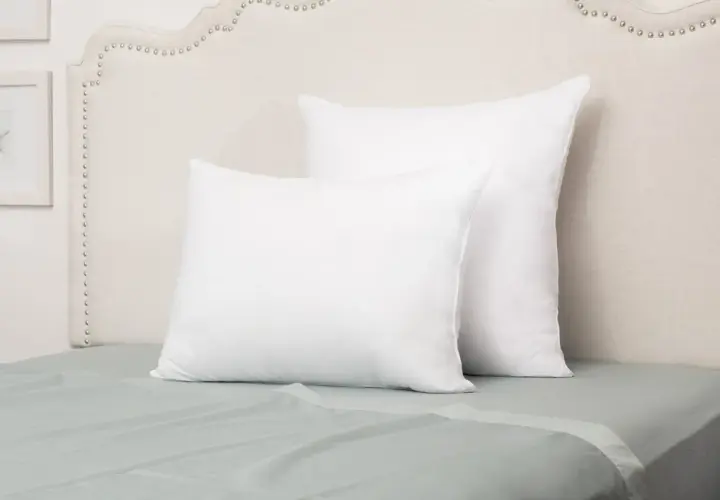 Two white pillows on a bed. The front pillow is a euro sham, while the larger one behind it is a standard sham, showcasing their size difference.