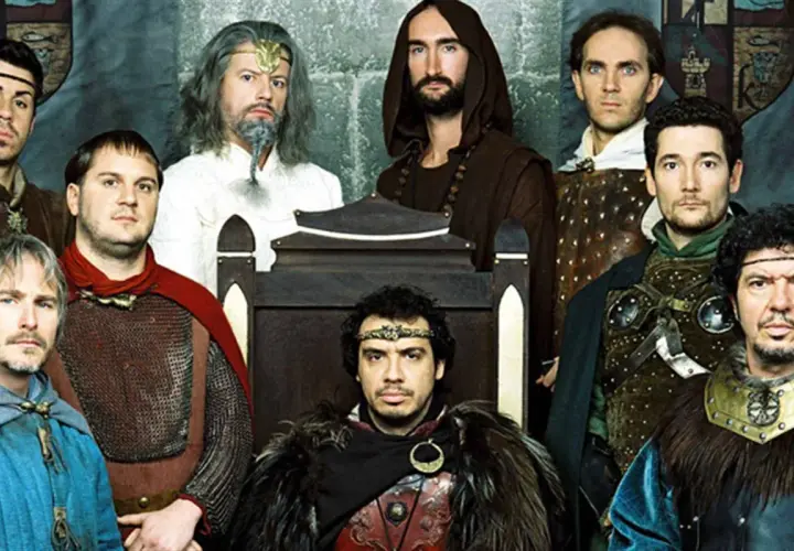 Le casting de Kaamelott réuni, des chevaliers aux allures diverses, certains sur un trône, d'autres en armure.