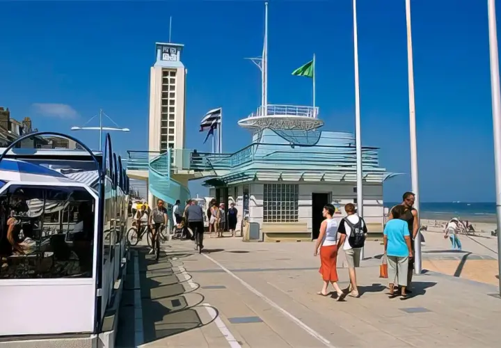 Promenade de Malo-les-Bains avec tramway, tour, bâtiments bleus et baigneurs sur la plage.