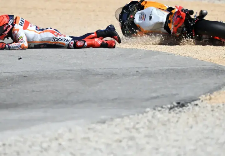 Piloto de MotoGP en el suelo tras una caída. La moto, volcada, derrapa en la grava. Un largo lap de competición que terminó mal.