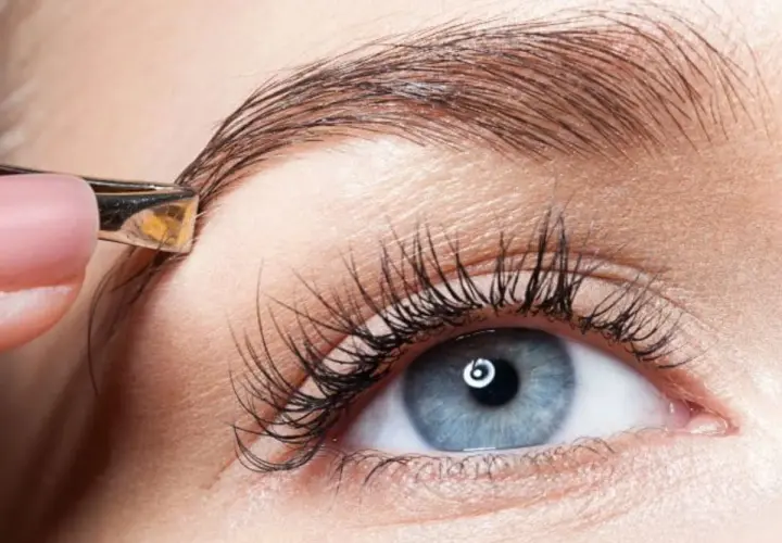 Une pince à épiler ajuste un sourcil. Un geste simple pour un dessin sourcil facile et un regard parfait.