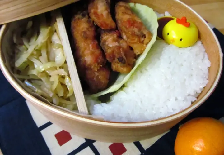 A delicious karaage bento box with crispy fried chicken, fluffy rice, pickled cabbage, and a cute chick-shaped decoration.